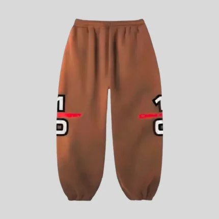 Brown relaxed-fit sweatpants with bold red, white and black graphic detailing across the outer legs, adjustable drawstring waist and elastic ankle cuffs.
